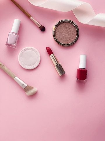 Smink och skönhetsprodukter som läppstift, nagellack och borstar på rosa bakgrund.